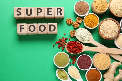 Photo of Different superfood products and words made of wooden cubes on green background, flat lay