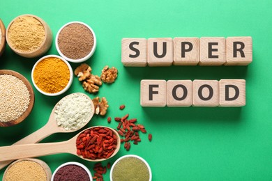 Photo of Different superfood products and words made of wooden cubes on green background, flat lay