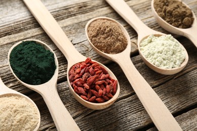 Photo of Different superfoods in spoons on wooden table, closeup