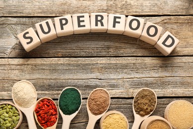 Photo of Different superfood powders and word made of cubes on wooden table, flat lay