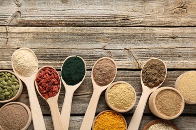Photo of Different superfoods in spoons and bowls on wooden table, flat lay. Space for text