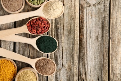 Photo of Different superfoods in spoons and bowls on wooden table, flat lay. Space for text