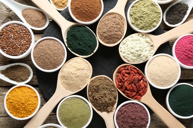 Photo of Different superfoods in spoons and bowls on wooden table, flat lay