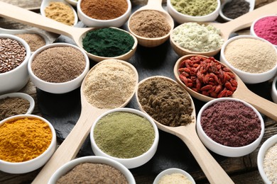 Photo of Different superfoods in spoons and bowls on table, closeup