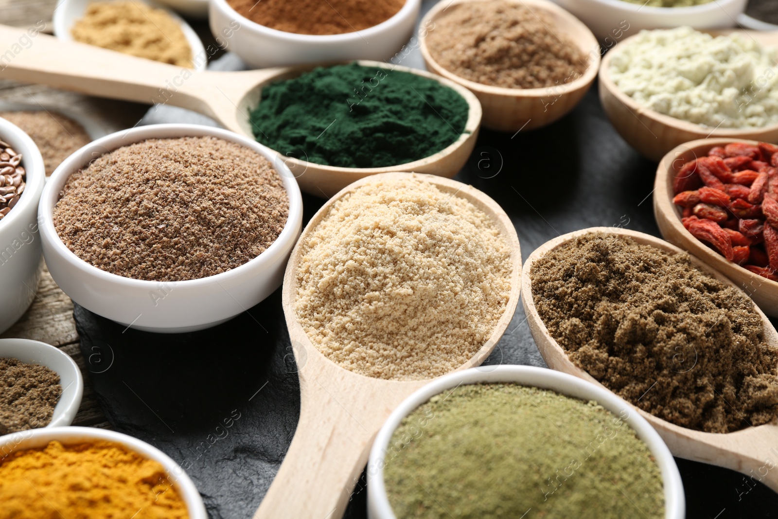 Different superfoods in spoons and bowls on black table, closeup Photo of Different superfoods in spoons and bowls on black table, closeup