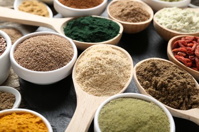 Photo of Different superfoods in spoons and bowls on black table, closeup