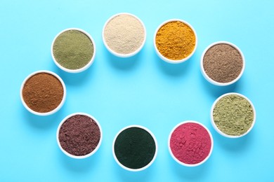 Photo of Frame of different superfood powders in bowls on light blue background, flat lay. Space for text