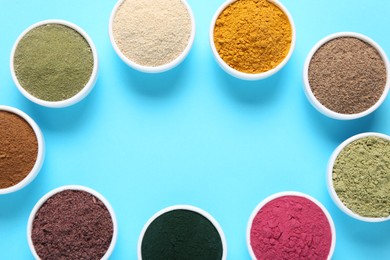 Photo of Frame of different superfood powders in bowls on light blue background, flat lay. Space for text