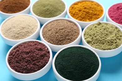 Photo of Different superfood powders in bowls on light blue background, closeup