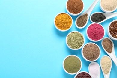 Photo of Different superfood powders in bowls and spoons on light blue background, flat lay. Space for text
