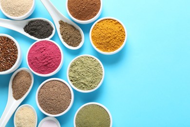 Photo of Different superfood powders in bowls and spoons on light blue background, flat lay. Space for text