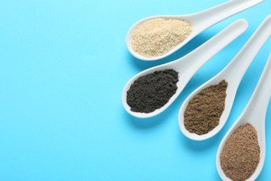 Photo of Different superfood powders in spoons on light blue background, flat lay. Space for text