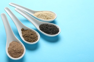 Photo of Different superfood powders in spoons on light blue background, closeup. Space for text