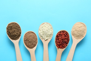 Photo of Different superfoods in spoons on light blue background, flat lay
