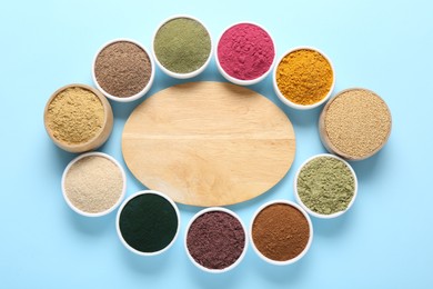 Photo of Different superfood powders in bowls and wooden board on light blue background, flat lay. Space for text