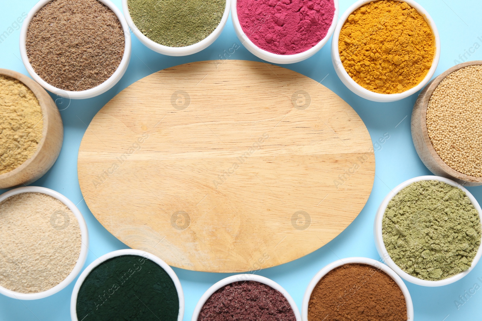 Different superfood powders in bowls and wooden board on light blue background, flat lay. Space for text Photo of Different superfood powders in bowls and wooden board on light blue background, flat lay. Space for text