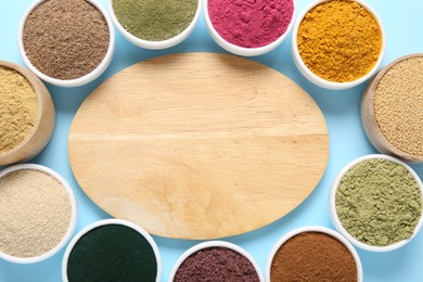 Photo of Different superfood powders in bowls and wooden board on light blue background, flat lay. Space for text
