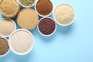 Photo of Different superfood powders in bowls on light blue background, flat lay. Space for text