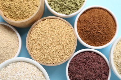 Photo of Different superfood powders in bowls on light blue background, flat lay