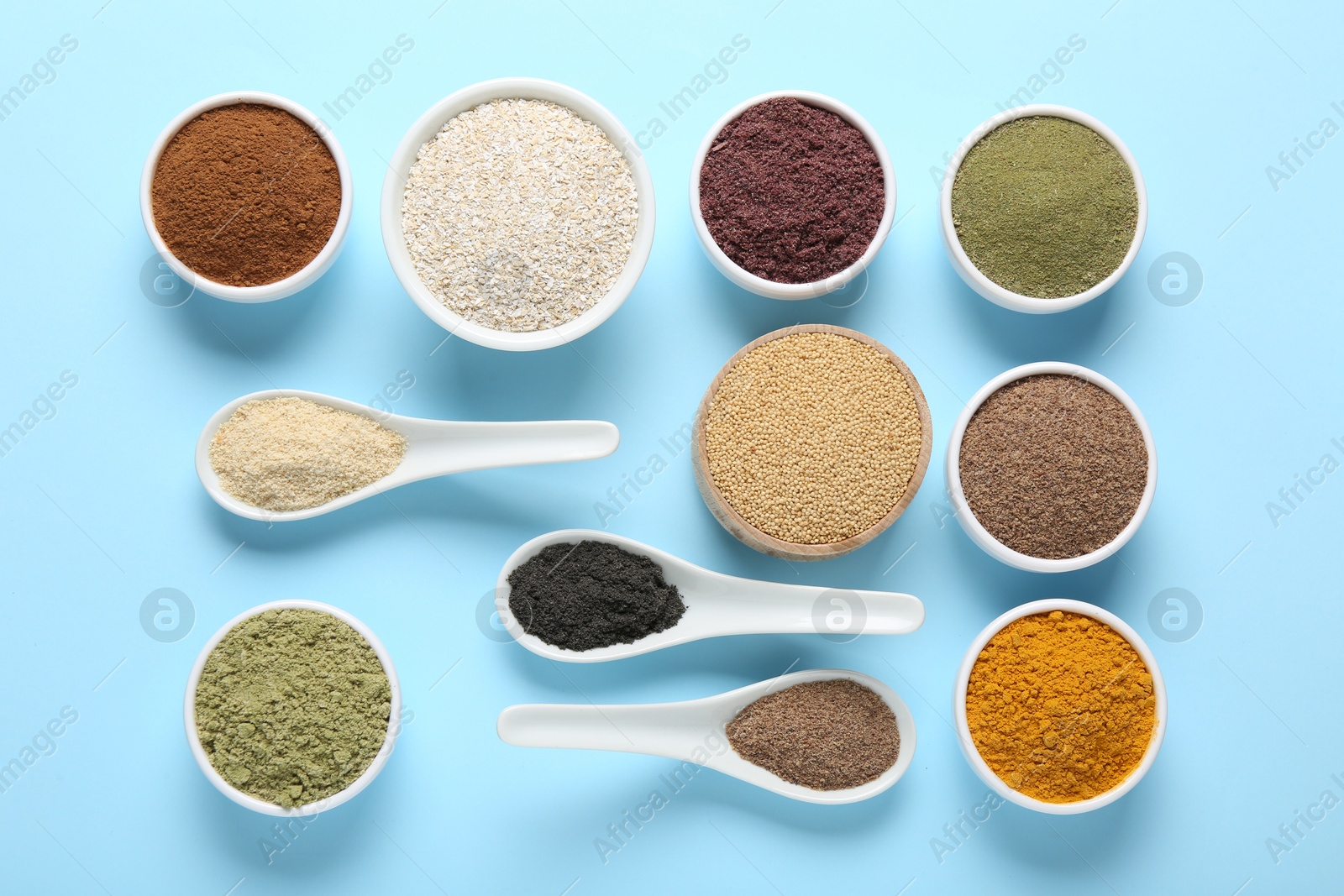 Different superfood powders in bowls and spoons on light blue background, flat lay Photo of Different superfood powders in bowls and spoons on light blue background, flat lay