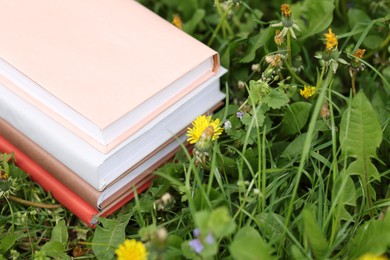 Photo of Stacked books on green grass outdoors, closeup. Space for text