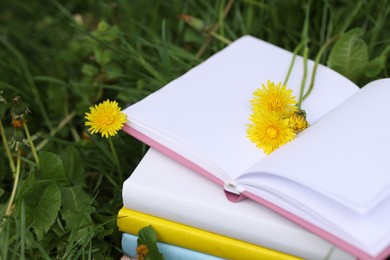 Photo of Stacked books with dandelion flowers on green grass outdoors, closeup