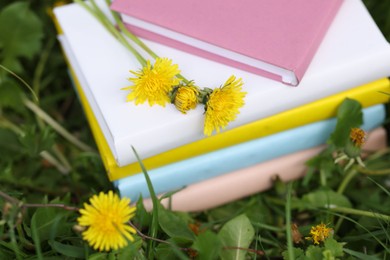 Photo of Stacked books with dandelion flowers on green grass outdoors, closeup