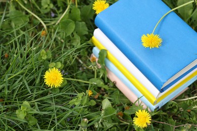Photo of Stacked books with dandelion flowers on green grass outdoors, closeup