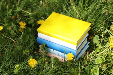Photo of Different stacked books on green grass outdoors