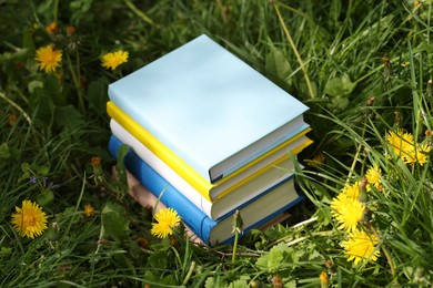 Photo of Different stacked books on green grass outdoors