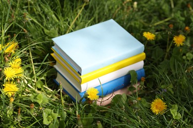 Photo of Different stacked books on green grass outdoors