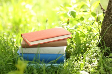 Photo of Different stacked books on green grass outdoors