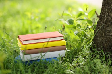Photo of Different stacked books on green grass outdoors