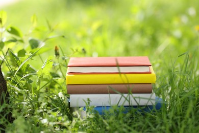 Photo of Different stacked books on green grass outdoors