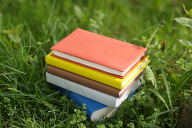 Photo of Different stacked books on green grass outdoors
