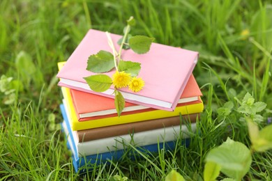 Photo of Stacked books with dandelion flowers on green grass outdoors, closeup