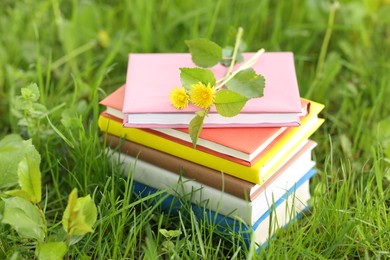Photo of Stacked books with dandelion flowers on green grass outdoors, closeup