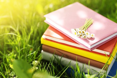 Photo of Stacked books with chamomile flowers on green grass outdoors, closeup