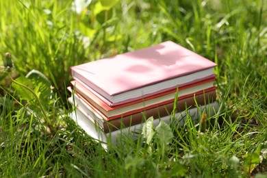 Photo of Different stacked books on green grass outdoors