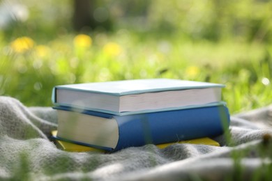 Photo of Stacked books and blanket on green grass outdoors, closeup