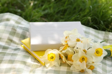 Photo of Stacked books, daffodil flowers and blanket on green grass outdoors, closeup