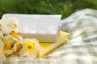 Photo of Stacked books, daffodil flowers and blanket on green grass outdoors, closeup