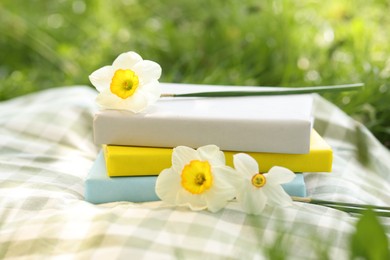 Photo of Stacked books, daffodil flowers and blanket on green grass outdoors, closeup