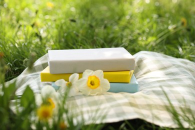 Photo of Stacked books, daffodil flowers and blanket on green grass outdoors, closeup