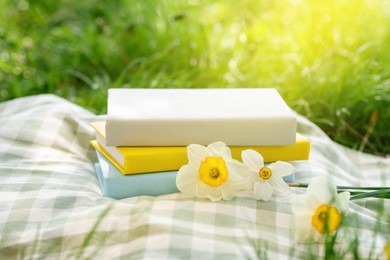 Photo of Stacked books, daffodil flowers and blanket on green grass outdoors, closeup