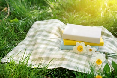 Photo of Stacked books, daffodil flowers and blanket on green grass outdoors