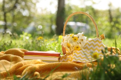 Photo of Stacked books, blanket and wicker basket with daffodil flowers on green grass outdoors