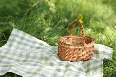 Photo of Wicker basket and blanket on green grass outdoors. Space for text