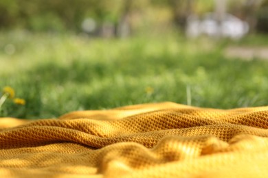 Photo of Orange blanket for picnic on green grass outdoors, closeup