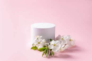Photo of Round podium and twig with beautiful flowers on pink background, closeup. Space for text